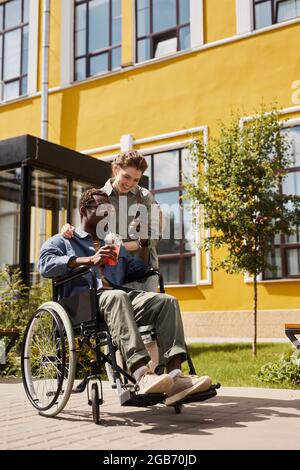 Disabled younh black man watching video on smartphone together with girlfriend while they walking in summer Stock Photo