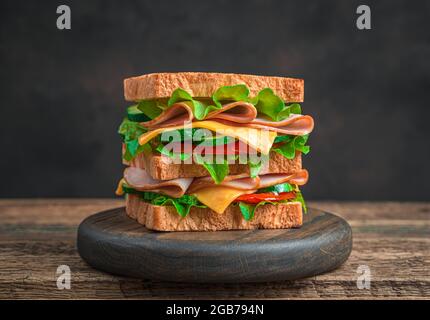 Club sandwich with ham, cheese, vegetables and salad on a brown background. Side view. Stock Photo