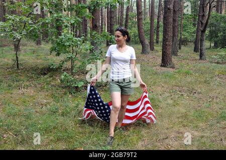 Young American woman holding an American flag on a forest background. Independence Day Stock Photo