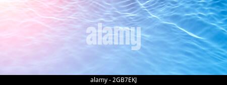 The reflection of light on the blue and pink transparent swimming pool water. Trendy abstract wavy background. Water waves in sunlight banner. Long Stock Photo