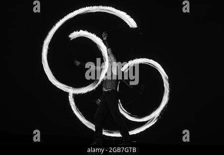 Fire poi artist perform burning reels with glowing, tails in motion on dark sky outdoors, stunt Stock Photo