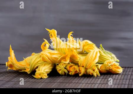 Raw zucchini flower concept:Fine dining cuisine of edible fresh and organic flowers. Healthy lifestyle ingredients. Yellow veggies on black background Stock Photo