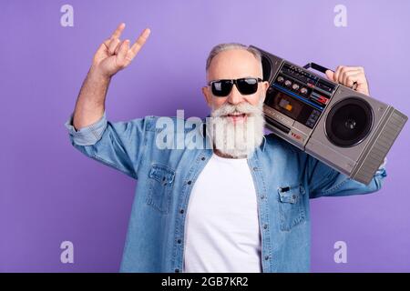 Photo of aged man happy positive smile hold boombox show fingers rock sign isolated over violet color background Stock Photo