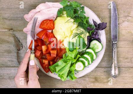 Female hand eating omlette with tomato, cucumber, herbs, ham, lettuce from plate on old wooden table Stock Photo