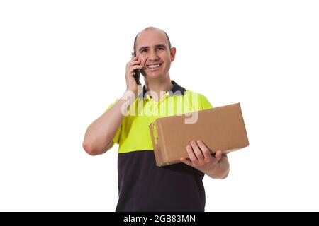 A smiling bald Caucasian man is holding a cardboard box with his left arm while with his right hand he holds his cell phone next to his ear as he is m Stock Photo