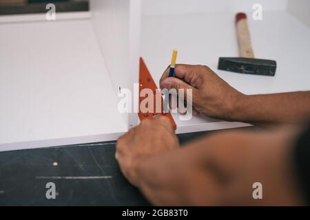 Hans of a man marking the point where make holes for screws in a piece of furniture Stock Photo