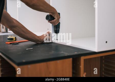 hands nailing a screw with a drill into a white wooden piece of furniture Stock Photo