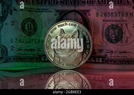 Doge cryptocurrency physical coin placed next to US dollar in the dark background and lit with green and red lights Stock Photo