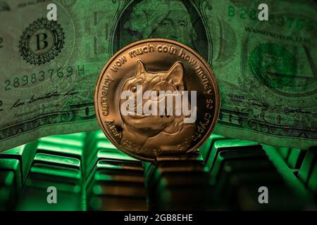 Doge cryptocurrency physical coin placed next to US dollar in the dark background and lit with green light Stock Photo