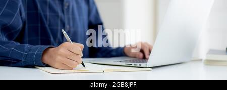 Closeup hand of business man writing on note while using laptop computer on desk at home, male planning on note for business success, author and blog, Stock Photo