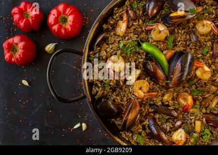 Black paella with seafood and squid ink with tomatoes on a black background Stock Photo