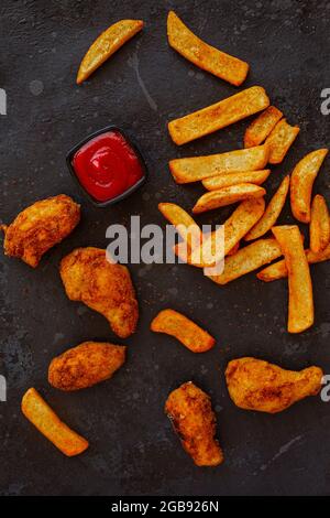 Spiced french potatoes and fried chicken with ketchup on a dark background Stock Photo
