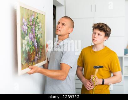 Son helps father to hang the painting on the wall of house Stock Photo