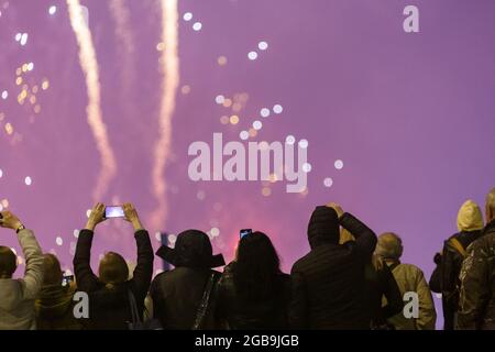 View from the back at people in wark clothes shooting fireworks on the phone at cold night. Stock Photo
