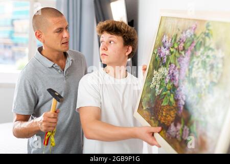 Son helps father to hang the painting on the wall of house Stock Photo