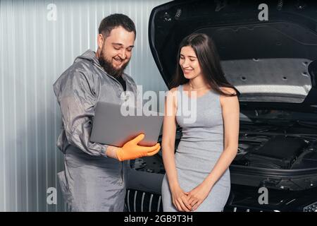 Car mechanic communicating with a yong customer while using laptop and examining vehicle at auto repair shop Stock Photo
