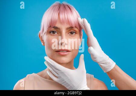 Hands of beautician examining female face before giving facial botox injections isolated over blue background Stock Photo