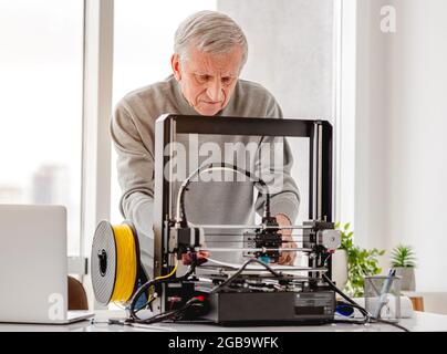 Adult man engineer working with 3D printer and preparing equipment for modeling Stock Photo