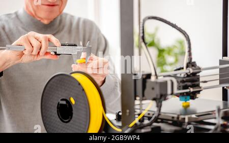 Man measuring size of yellow detail printing with modern 3D printer using professional tools Stock Photo