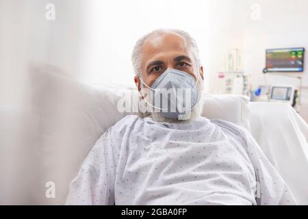 AN OLD MAN WEARING FACE MASK LOOKING AT CAMERA WHILE RESTING Stock Photo