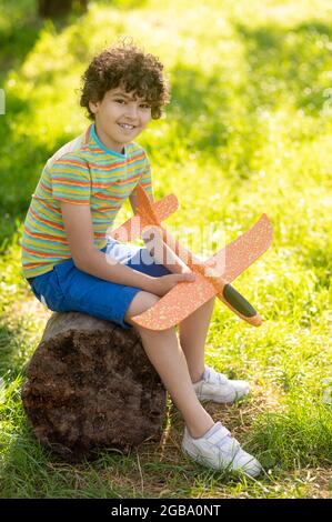 Boy with toy plane sitting on tree stump Stock Photo