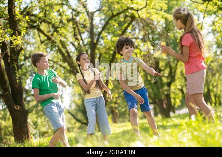 Cheerful boys and girls with soap bubbles in park Stock Photo