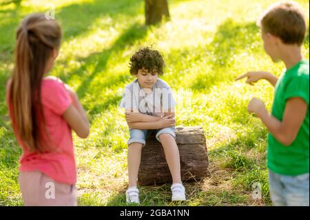 Pensive boy sitting on tree stump and friends Stock Photo