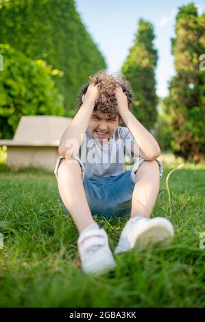 Boy holding his head sitting on the grass Stock Photo