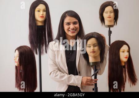A YOUNG HAIR STYLIST HAPPILY POSING WITH DUMMY HAIR Stock Photo