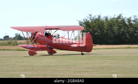 Ferrara Italy JUNE, 27, 2021 Red vintage biplane from the 1930s parked in a grass airfield in the countryside. WACO UPF7 Stock Photo