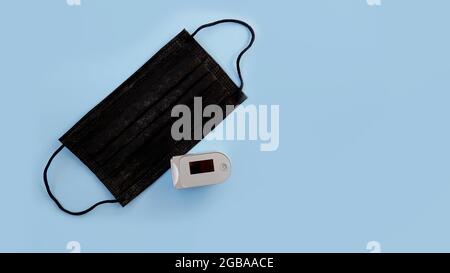 Medical black mask and oximeter on a blue background. Copy space. Stock Photo