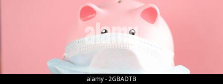 Pink pig piggy bank in protective mask and stethoscope stands on table Stock Photo