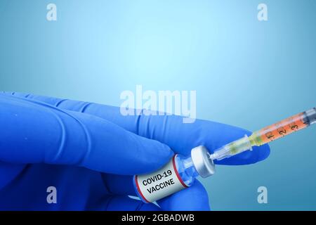Health worker hand with gloves holding syringe and covid 19 vaccines with colored background Stock Photo