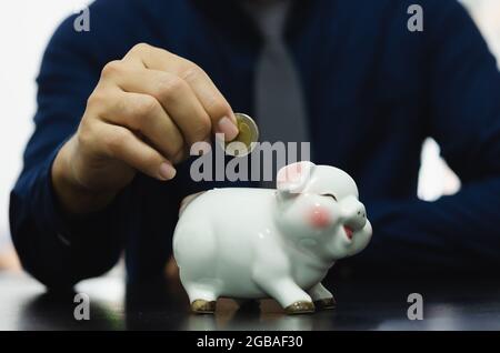 Saving money drops the piggy bank for investment or buying a fund or using it in an emergency. Men's hands are dropping money at the piggy bank. Finan Stock Photo