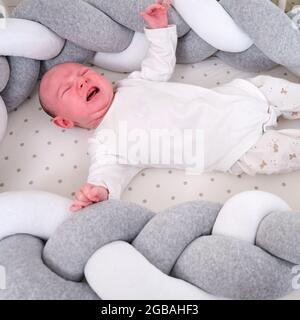 Portrait of a baby boy aged one month crying in a crib. Caucasian screaming child in the children bedroom on the bed Stock Photo