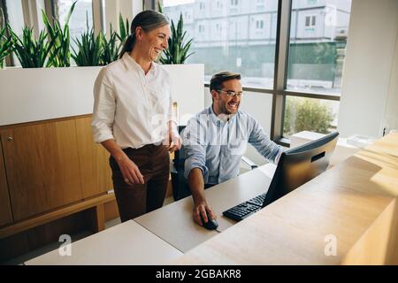 Happy female executive supervising her coworker work on computer. Manager and employee looking at computer and smiling. Stock Photo