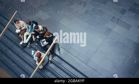 High angle view of university students sitting on stairs and discussing studies. Young people studying in college campus. Stock Photo