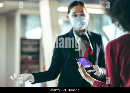 Woman passenger holding smart phone with boarding pass standing at airport check-in counter. Woman checking in using digital boarding pass at airport Stock Photo