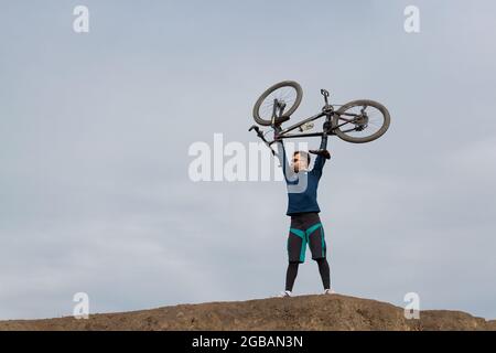 Bearded cyclist on the mountain holds his bike in his arms above his head Stock Photo