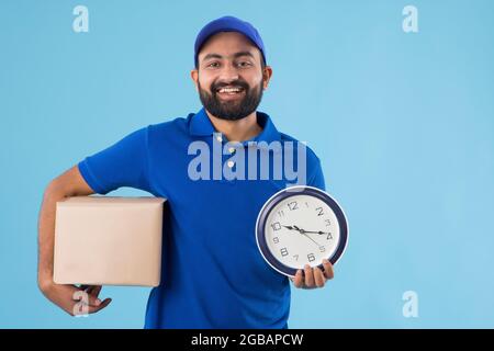 A HAPPY BEARDED DELIVERY GUY HOLDING A PARCEL AND CLOCK IN HAND Stock Photo