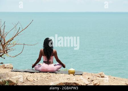 Fit young woman meditating in lotus position and looking at calm beautiful seascape Stock Photo