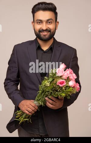 A WELL-GROOMED YOUNG MAN STANDING WITH BOUQUET IN HAND Stock Photo