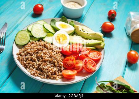 Vegan lunch bowl with avocado, egg, cucumber, tomato and buckwheat on wooden background Stock Photo