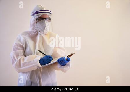 A health worker in PPE kit writing in notepad with a pen. Stock Photo