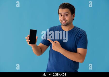 A young man pointing towards mobile phone in his hands. Stock Photo