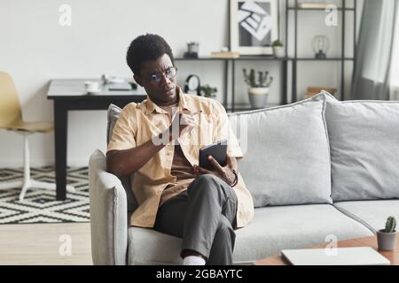 African young man relaxing on sofa and watching something online on digital tablet in the room at home Stock Photo