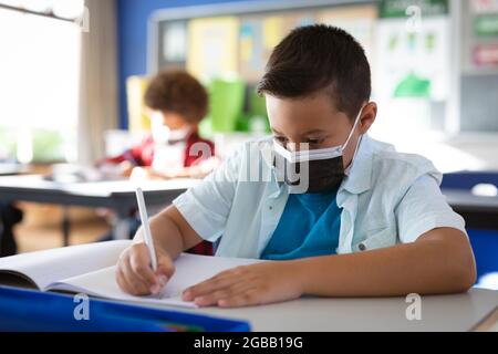 Caucasian boy wearing face mask studying while sitting on her desk in the class at school Stock Photo
