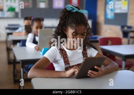 African american girl using digital tablet while sitting on her desk in the class at school Stock Photo