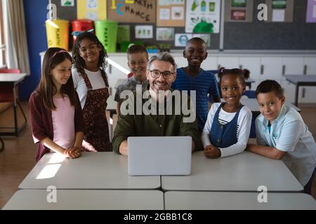 Portrait of caucasian male teacher and group of diverse students with laptop in the class at school Stock Photo
