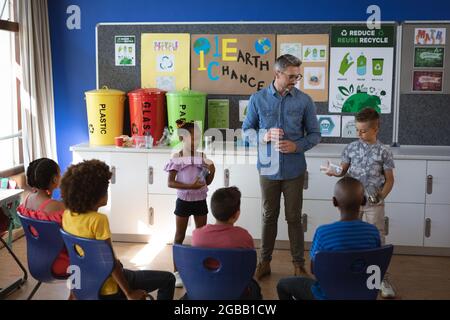 Caucasian boy and african american girl showing how to recycle plastic items to students at school Stock Photo
